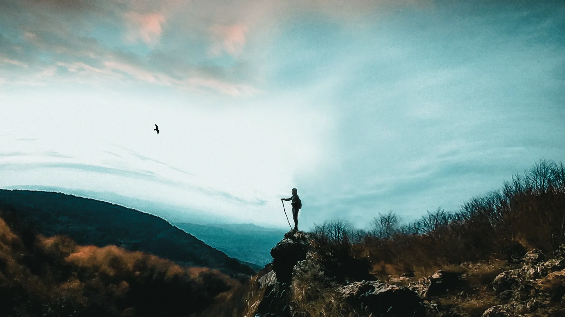 A lone hiker standing on a ridge beneath a wide sky.