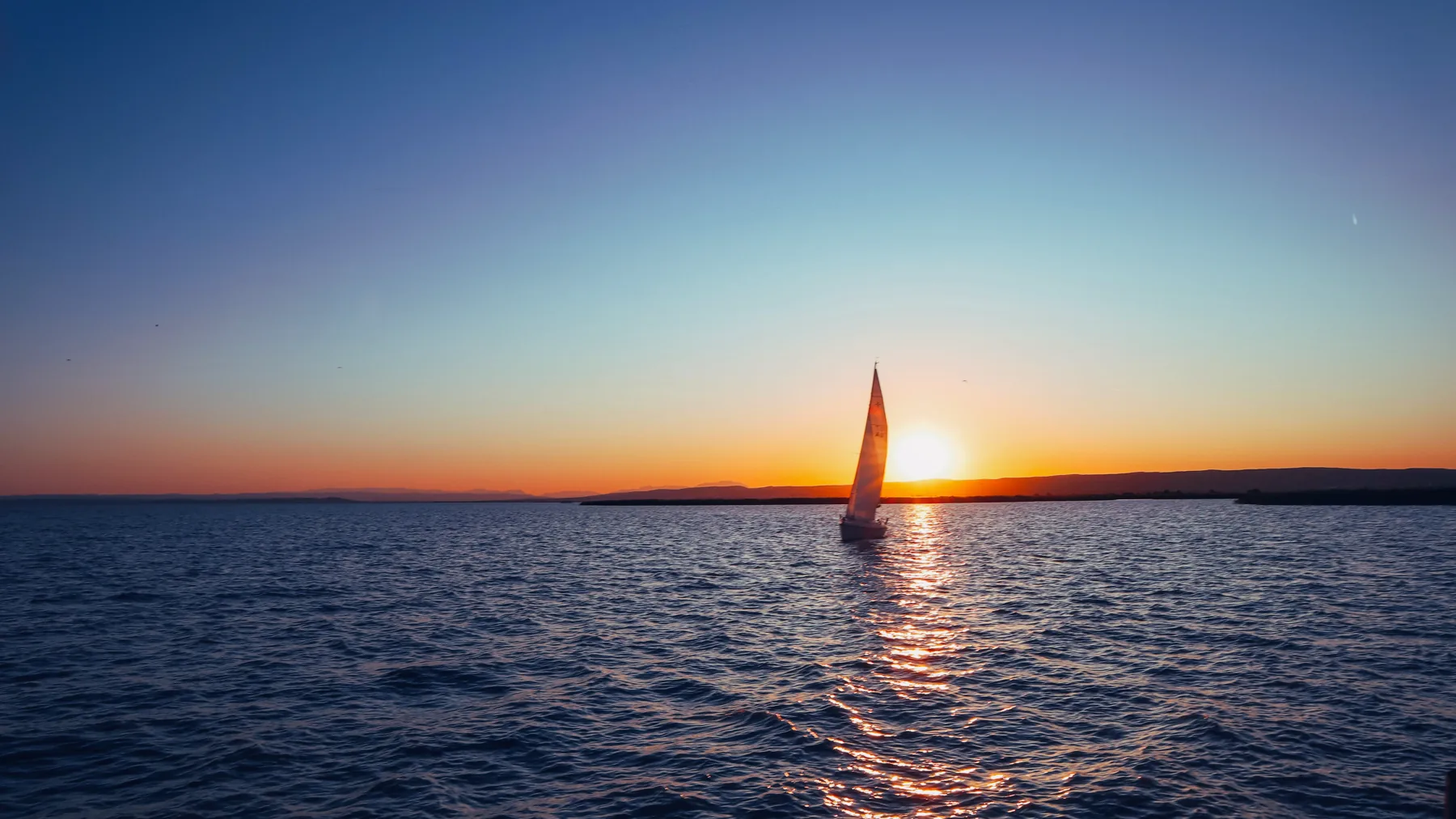 A sailboat crossing open water at sunset.